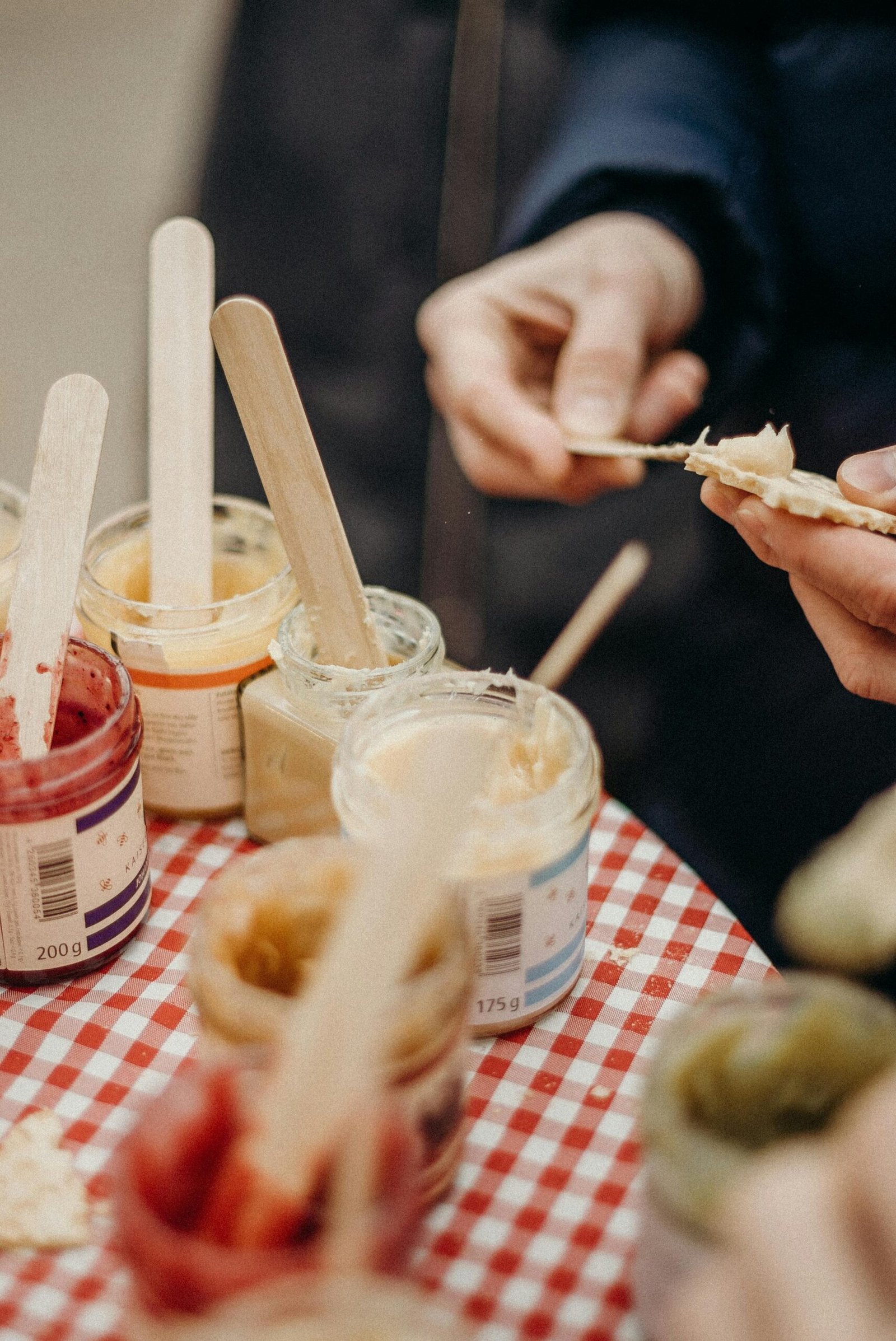 Multiple jars of vibrant jams with wooden sticks on a market table.