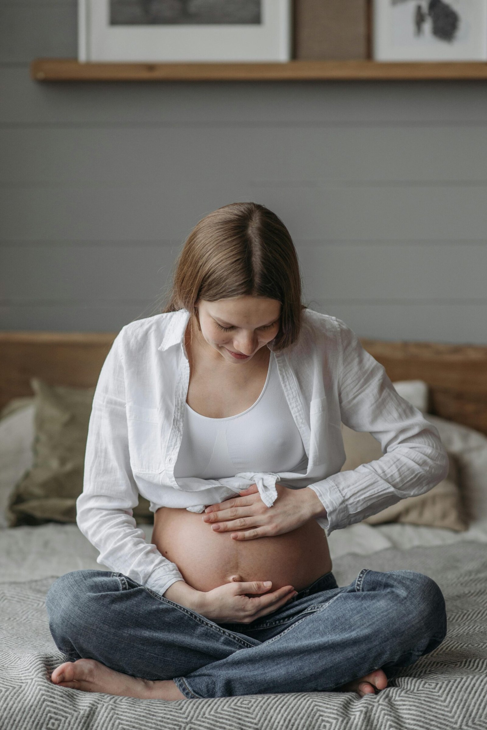 A serene portrait of a pregnant woman sitting on a bed, gently holding her baby bump.