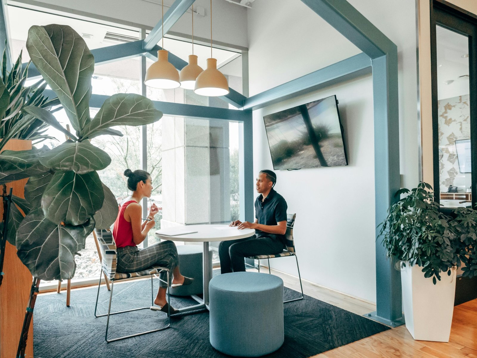 Two colleagues in a modern office space having a discussion with indoor plants and stylish decor.